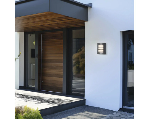 Moderní fasáda domu s osvětleným nástěnným svítidlem vedle vchodových dveří.