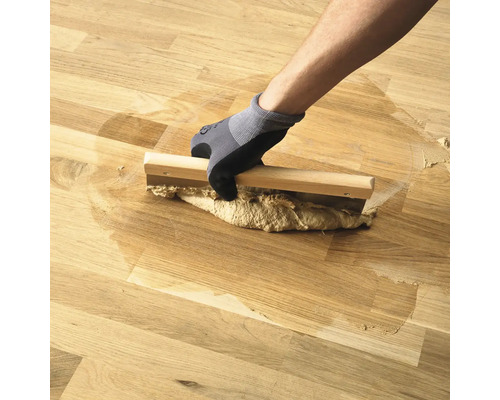 Řemeslník nanáší dřevěný tmel na dřevěnou podlahu pomocí dřevěné špachtle
