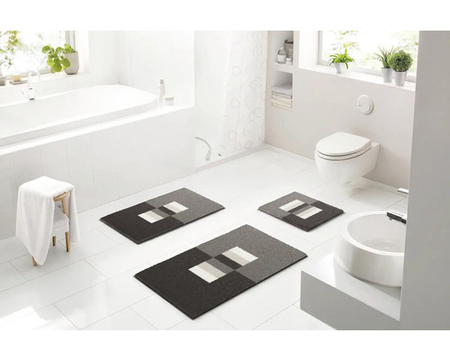 Světlá koupelna s vanou, umyvadlem, toaletou a sadou tří koupelnových koberečků s geometrickým vzorem