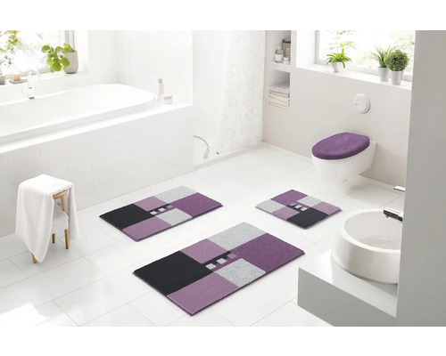 Světlá koupelna s vanou, umyvadlem, toaletou a sadou koupelnových předložek ze tří kusů s geometrickým vzorem