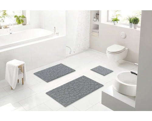 Světlá koupelna s vanou, umyvadlem, toaletou a šedou sadou koupelnových předložek.