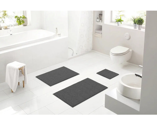 Světlá koupelna s vanou, toaletou, umyvadlem a třemi šedými koupelnovými koberci