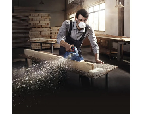 Muž používá elektrický hoblík na dřevěné desce v dílně.