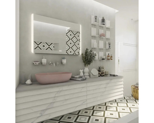 Světlá koupelna s růžovým umyvadlem, osvětleným zrcadlem a dekorativními policemi.