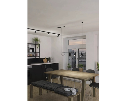 Moderní kuchyně s černou kuchyňskou linkou, dřevěným stolem, lavicí s polštáři a kolejnicovým systémem se spoty pro osvětlení