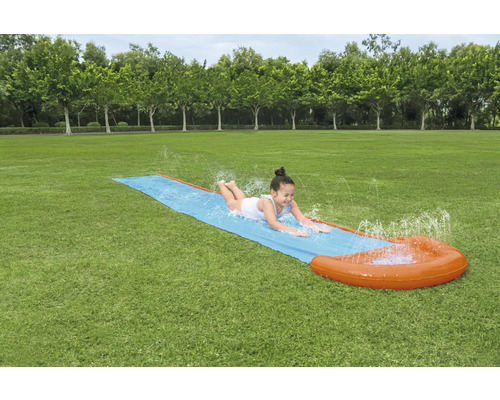 Dívka klouže na vodní skluzavce na zahradě