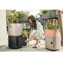 Scéna na balkóně se dvěma květináči se zavlažovacím systémem, na kolečkách a s úložným prostorem, žena zalévá rostliny