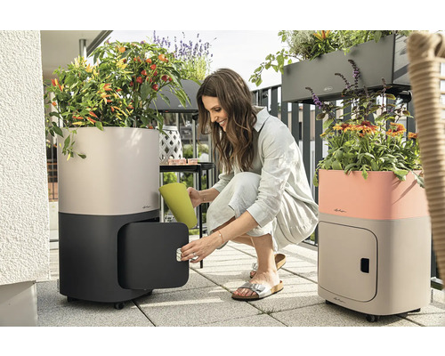 Scéna na balkóně se dvěma květináči se zavlažovacím systémem, na kolečkách a s úložným prostorem, žena zalévá rostliny