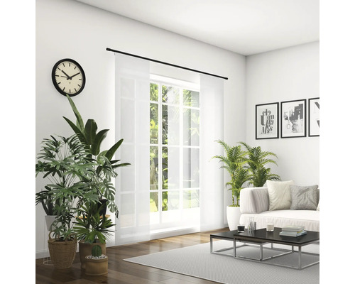 Světlý obývací pokoj s pohovkou, konferenčním stolkem, pokojovými rostlinami, hodinami a posuvným závěsem před oknem.