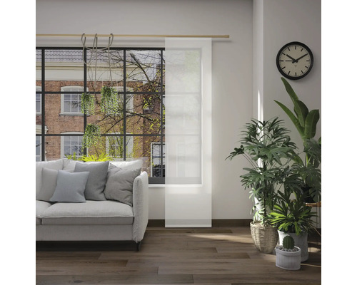 Obývací pokoj s pohovkou, pokojovými rostlinami, hodinami a posuvným panelem před oknem