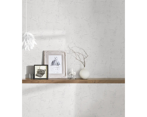 Světlá místnost s bílou strukturovanou tapetou, zdobená policemi, obrázky a lampou.