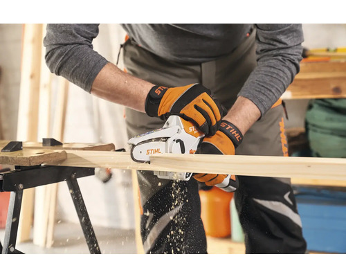 Osoba řeže dřevěnou desku akumulátorovou motorovou pilou.