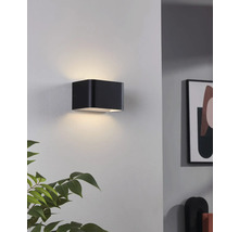 Černé nástěnné svítidlo ve tvaru krychle osvětluje zeď