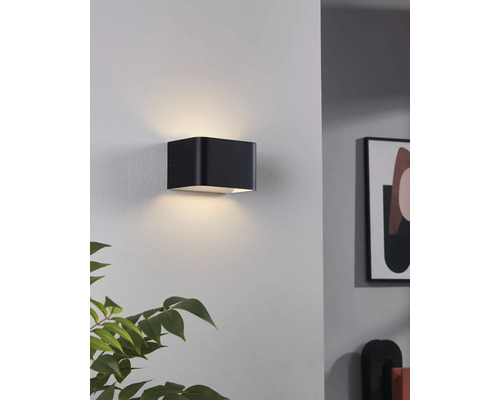 Černé nástěnné svítidlo ve tvaru krychle osvětluje zeď