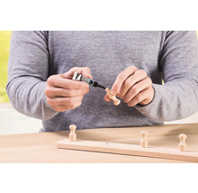Osoba přilepuje dřevěný háček na dřevěnou lištu lepidlem