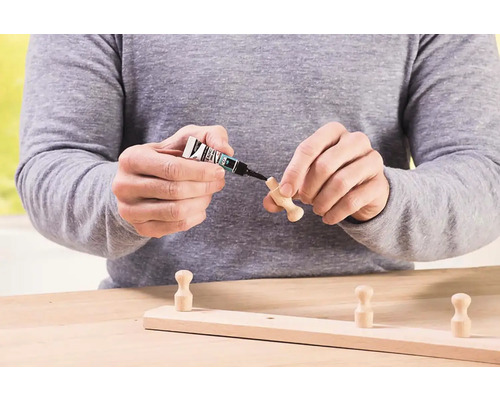 Osoba přilepuje dřevěný háček na dřevěnou lištu lepidlem