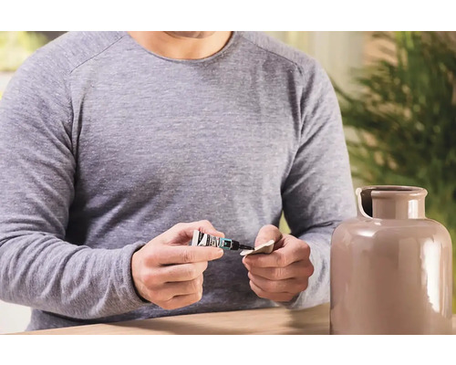 Muž opravuje keramickou vázu lepidlem