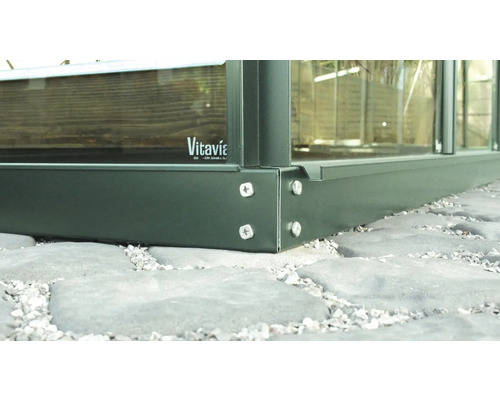 Detailní pohled na skleník s hliníkovým rámem a skleněnými panely na kamenné podlaze. Logo Vitavia.