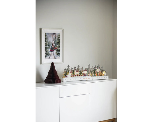 Dekorativní vánoční scéna s osvětlenou zimní krajinou, papírovým stromem a obrázkem vlaku na bílé skříňce