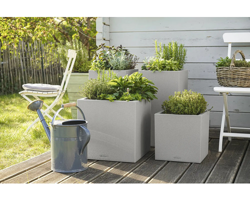 Tři čtvercové květináče s bylinkami a konev na zahradě