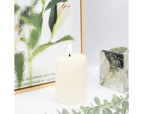 Dekorativní LED sloupková svíčka s malbou v pozadí a mramorovaným svícnem.