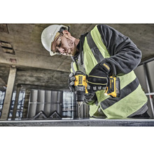 Pracovník s ochrannou přilbou vrtá vrtačkou DeWalt do kusu kovu.