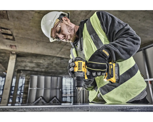 Pracovník s ochrannou přilbou vrtá vrtačkou DeWalt do kusu kovu.
