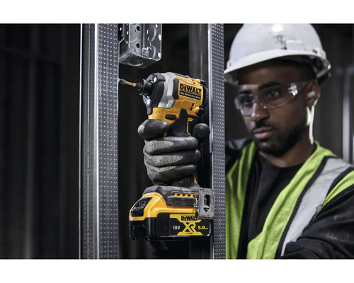 Muž s ochrannými brýlemi a helmou šroubuje žlutým akumulátorovým rázovým utahovákem DeWalt šroub do kovového profilu