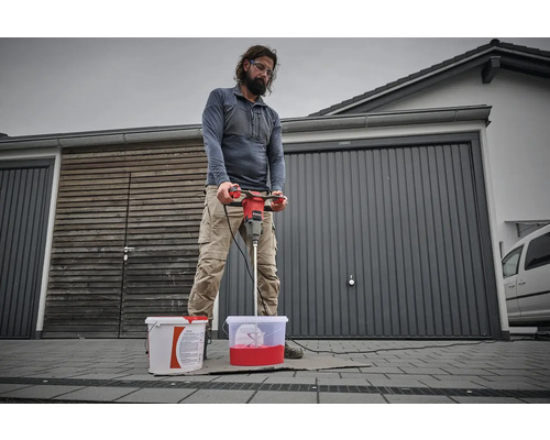 Muž míchá barvu s míchadlem barev před garáží