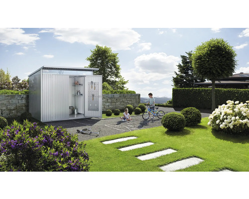 Kovový zahradní domek s otevřenými dveřmi, policemi a nářadím v zahradě s hrajícími si dětmi.