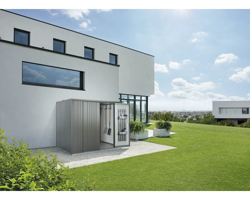 Kovový zahradní domek s otevřenými dveřmi a zahradním nářadím před moderním domem