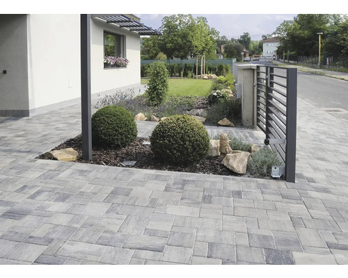 Příjezdová cesta s dlažebními kostkami, zahradním plotem a výsadbou.
