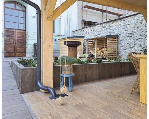 Exteriér s terasovou dlažbou ve vzhledu dřeva, skladem dřeva a truhlíky na rostliny