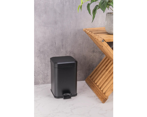 Černý kovový odpadkový koš vedle dřevěné stoličky s rostlinou