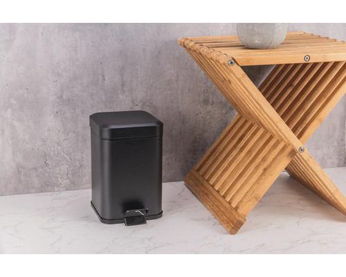 Černý kovový odpadkový koš vedle dřevěné stoličky.