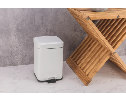 Bílý kovový pedálový koš vedle dřevěné stoličky