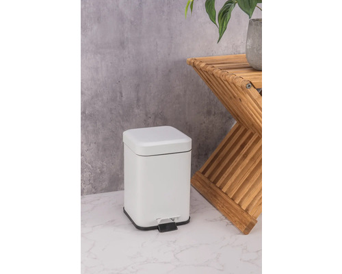 Bílý kovový odpadkový koš s pedálem vedle dřevěného odkládacího stolku