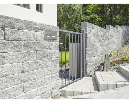 Pohled do zahrady se zdí z kamenných bloků a kovovou bránou