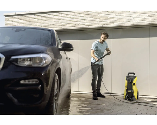 Muž čistí auto pomocí tlakové myčky.