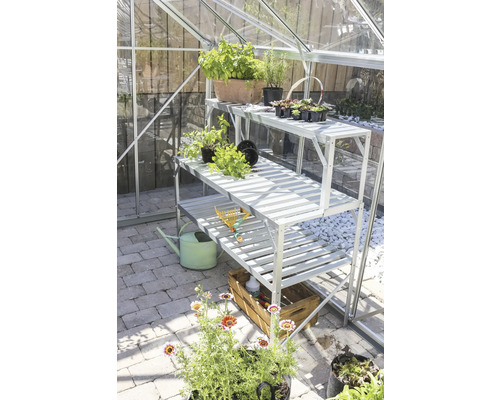 Skleník s třípatrovým regálem, rostlinami a zahradním příslušenstvím.