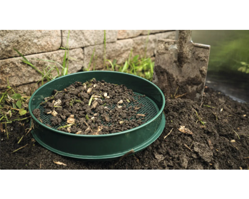 Zahradní síto s hlínou a lopatou na zahradě