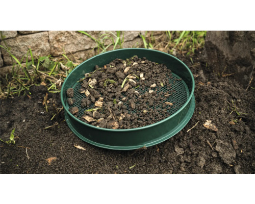 Zahradní síto s hlínou a zbytky rostlin na zemi