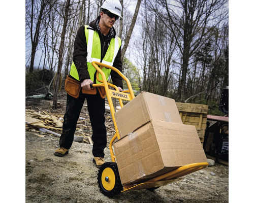 Stavební dělník přepravuje kartony rudlem na staveništi. Rudl je žlutý a má logo DeWalt.