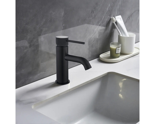 Černá umyvadlová baterie vedle bílého umyvadla a koupelnových potřeb