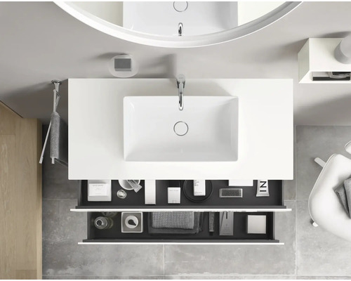 Pohled shora na koupelnu s umyvadlem, umyvadlovou skříňkou, zrcadlem a otevřenými zásuvkami.