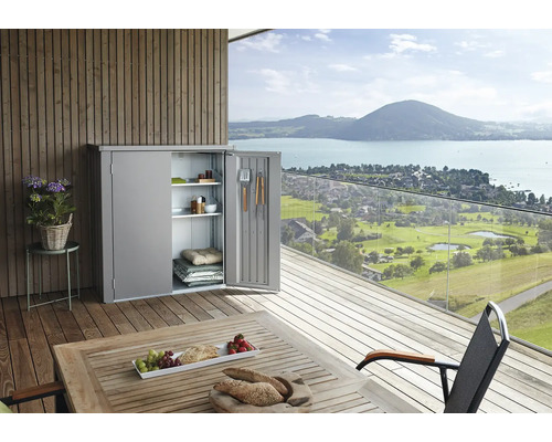 Kovová zahradní skříňka s otevřenými dveřmi na terase s výhledem na jezero a hory