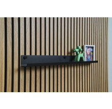 Černá nástěnná police před dřevěnou obkladovou stěnou s dekorací