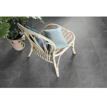 Scéna s ratanovým křeslem s polštáři a hrnkovou rostlinou na šedé podlaze.