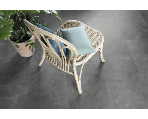 Scéna s ratanovým křeslem s polštáři a hrnkovou rostlinou na šedé podlaze.