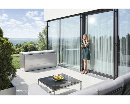 Scéna s kovovým úložným boxem na terase, stolem a ženou, která jí hrozny